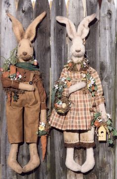 two stuffed rabbits are standing next to each other in front of a wooden fence with flowers