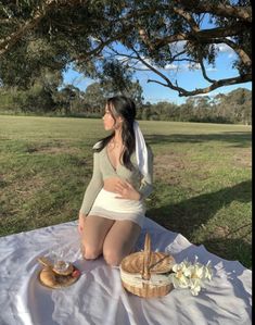 a woman sitting on top of a white blanket next to a picnic basket and bread