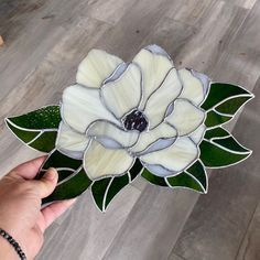 a hand holding a stained glass flower on top of a wooden floor next to a wall