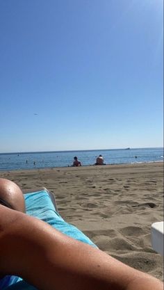 a woman laying on top of a blue towel next to the ocean with people in the background