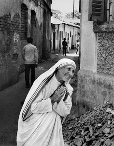 an old woman is walking down the street in front of some buildings with people standing around her