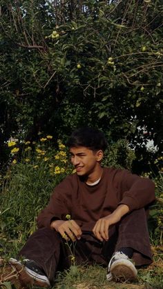 a man sitting on the ground in front of some bushes