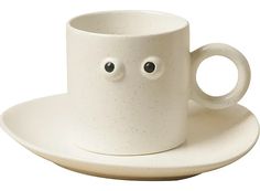 a white coffee cup with googly eyes and saucer sitting on top of a plate