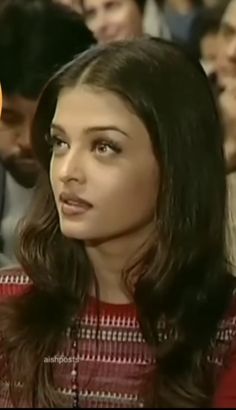 a woman with long hair sitting in front of a group of people and looking off to the side