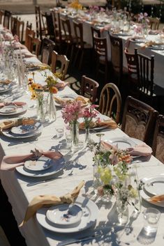 a long table is set with plates and flowers in vases on the tablescloth