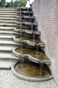 several water fountains are lined up against a brick wall in front of steps and stairs