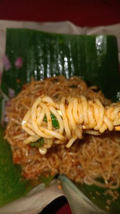 some noodles are being held up by a fork on top of a leafy green plate