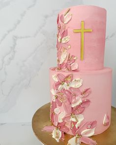 a pink cake decorated with white flowers and a cross on the top is sitting on a gold platter