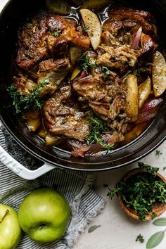 a pot filled with meat and potatoes on top of a table next to an apple