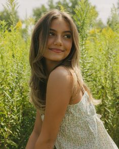 a beautiful young woman standing in front of tall grass