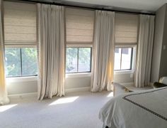 a bedroom with white carpet and two windows that have curtains on the side of them