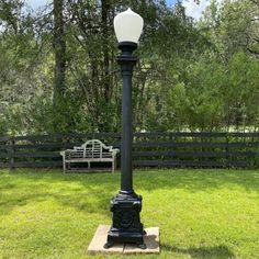 an old fashioned lamp post in the middle of a grassy area next to a park bench