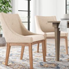 two beige chairs sitting on top of a rug next to a wooden table and chair