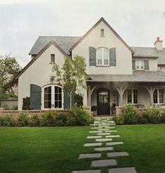 a white house with green shutters and stone steps leading to the front door on a cloudy day