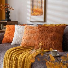 a couch with orange and white pillows on top of it next to a coffee cup