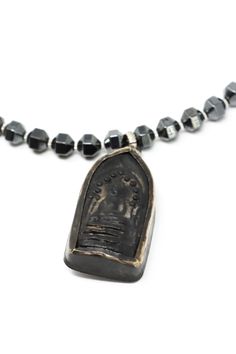 The Mya Lambrecht Buddha Necklace is minimal yet striking! Material: Natural stones, metalOrigin: Made in Minnesota Hook closure Handmade sitting Buddha from Thailand Ancient Chinese I-Ching coin Hematite 28" long Mya Lambrecht incorporates everyday objects into her pieces that are seemingly out of place. Her pieces create a relationship between people and the earth. Oxidized Pendant For Meditation, Handmade Brass Spiritual Coin Necklace, Oxidized Finish Pendant For Meditation, Spiritual Bronze Jewelry With Oxidized Finish, Hand Forged Amulet Necklace With Round Pendant, Symbolic Oxidized Finish Necklace For Meditation, Spiritual Oxidized Finish Jewelry For Meditation, Bronze Amulet Necklace With Oxidized Finish, Spiritual Hand Forged Medallion Necklaces