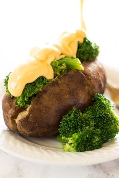 a white plate topped with broccoli covered in cheese sauce next to a baked potato