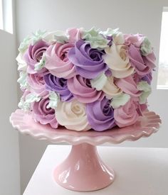 there is a pink cake with purple and white flowers on the top, sitting on a pedestal