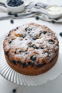 a cake sitting on top of a glass plate next to blueberries and cream cheese