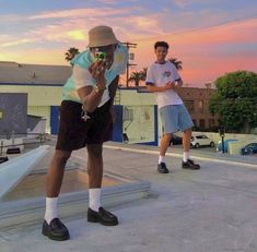 two men standing on top of a roof next to each other while the sun sets