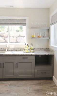 a kitchen with gray cabinets and marble counter tops, along with open shelves on the wall