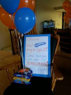 a sign that is on top of a chair with balloons in the air and some candy