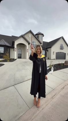 a woman standing in front of a house holding up a yellow object with one hand