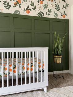 a white crib in front of a green wall with oranges and leaves on it