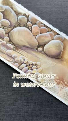 a painting with rocks and sand in it on top of a black tablecloth that says painting stones in watercolour