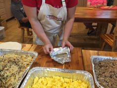 a person in an apron preparing food on top of a wooden table with tin foil