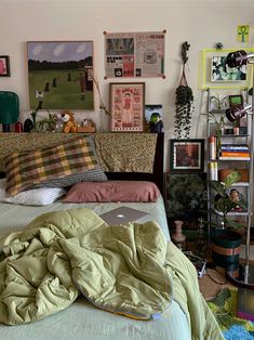 an unmade bed in a bedroom with pictures on the wall above it and a laptop computer