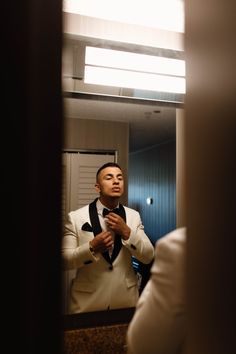 a man in a white tuxedo looking at himself in the mirror