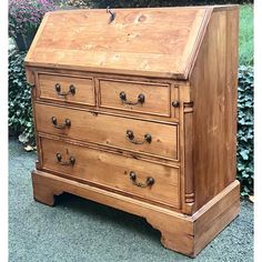 an old fashioned wooden desk with drawers and knobs on the bottom, sitting in front of some bushes