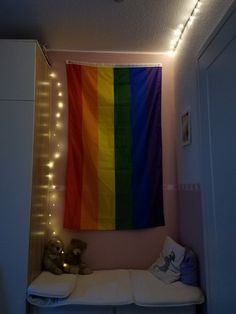 there is a rainbow flag hanging on the wall above a bed with pillows and stuffed animals