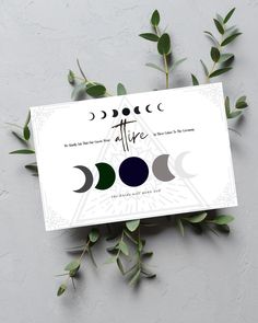 a card with three phases of the moon on it and some green leaves around it