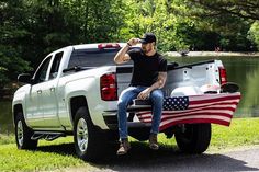 a man sitting on the back of a truck with an american flag in the bed