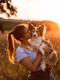 a woman holding a small dog in her arms while the sun is setting behind her