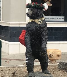 a statue of a black bear wearing a christmas wreath on its head is in front of a building