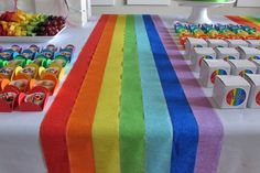 there is a rainbow table with candy on the table and other sweets in boxes next to it