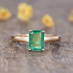 an emerald ring sitting on top of a piece of wood with yellow flowers in the background