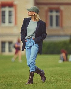 a woman standing in the grass with her hands on her hips wearing boots and a hat