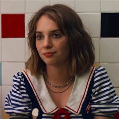 a woman wearing a striped shirt with a red tie around her neck, sitting in front of a tiled wall