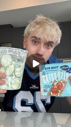 a young man holding up a box of frozen cucumbers in front of him