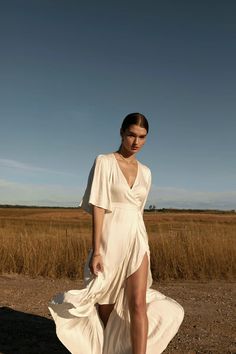 a woman in a white dress is walking on the dirt road with her legs crossed