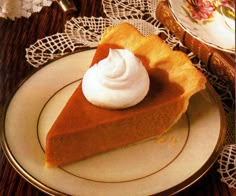 a slice of pumpkin pie with whipped cream on top sits on a plate next to a lace doily