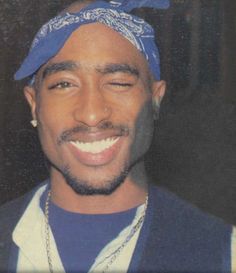 a man with a blue bandana on his head smiling at the camera while wearing a necklace