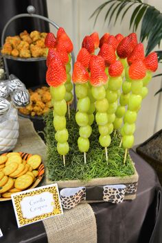 grapes and strawberries are arranged on sticks in front of other desserts at a party