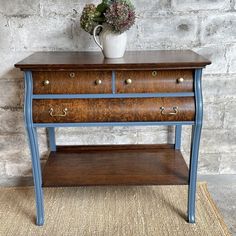 an old wooden table with drawers and a vase on top, against a brick wall