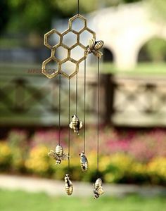 a wind chime with bees hanging from it's sides in front of flowers