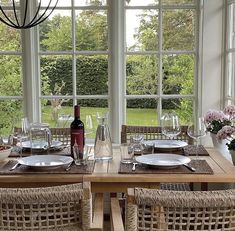 a dining room table set with place settings and wine bottle on the table in front of large windows